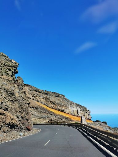 A vertical shot of an empty road under a sunny blue sky in La Palma island, Spain