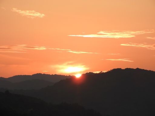 A beautiful shot of the sun setting behind hills with a bright orange sky
