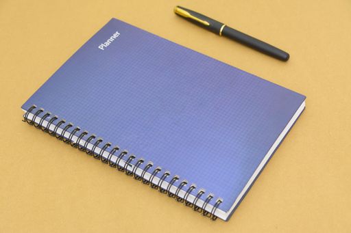 A closeup shot of notebook with a ballpen beside it on a brown background