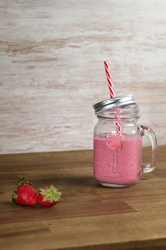 A vertical shot of a fresh healthy fruit smoothie and two strawberries on a clear wooden background