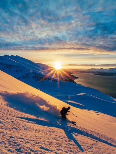A vertical shot of a guy skiing down the snowy mountain at sunset in daylight