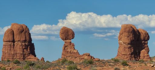 A scenic view of rock formations in a desert covered with green shrubs in Arches National Park