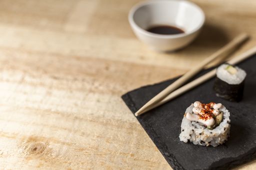 A high angle closeup shot of three sushi pieces with sticks and soy sauce on a wooden table
