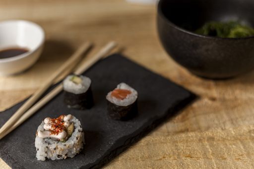 A high angle closeup shot of three sushi pieces with sticks and soy sauce on a wooden table