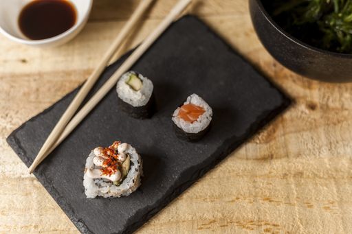 A high angle closeup shot of three sushi pieces with sticks and soy sauce on a wooden table