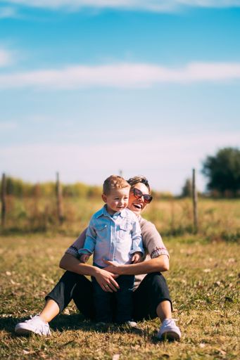 A shallow focus vertical shot of a cute boy and his mother sitting on the grass on a sunny day
