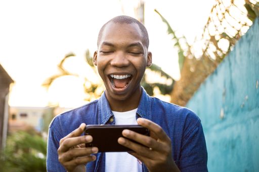 A shallow focus of a cheerful African American male watching a video on his phone under the sunlight