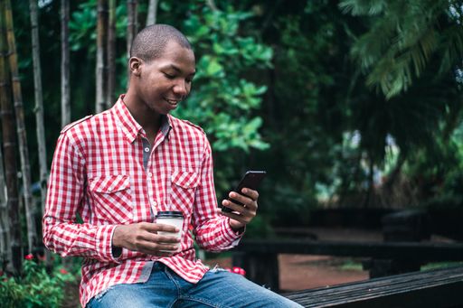 A shallow focus of a young African American male in a red and white chequered shirt using his phone in a park