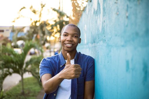 A shallow focus of a young African American male in a blue shirt doing the thumbs-up gesture in a park