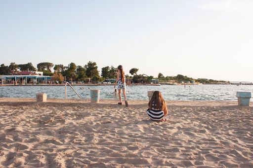 Two girls from behind near the sandy beach with lush green trees in the background