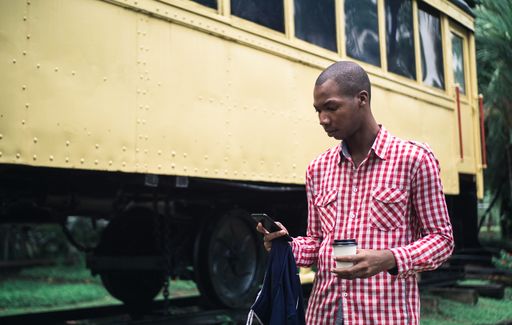 A shallow focus of a young African American male in a red and white chequered shirt using his phone in a park