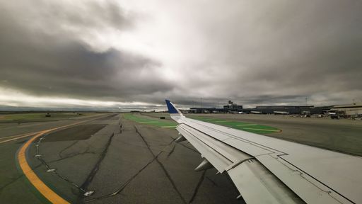 A shot from inside a plane of its wing in the airport on a cloudy day