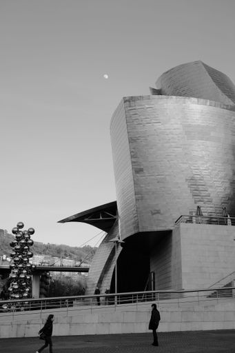 A vertical shot of Guggenheim Museum Bilbao in black and white with the moon in the background