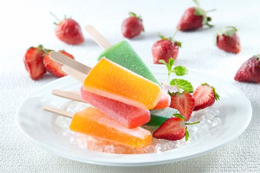A closeup of colorful frosty ice creams with various flavors on a plate with ice and strawberry