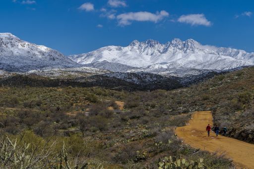 The image shows a view of the snow capped mountains in the Sonoran desert with two figures in the distance walking toward the mountains
