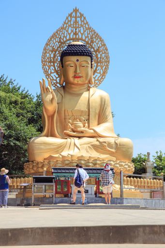 A vertical shot of tourists near a large golden Buddha statue at the Sanbanggulsa Temple in Jeju, Korea