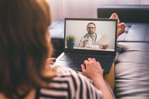 Woman lying on a sofa at home and talking with a doctor online using laptop. Telemedicine concept.