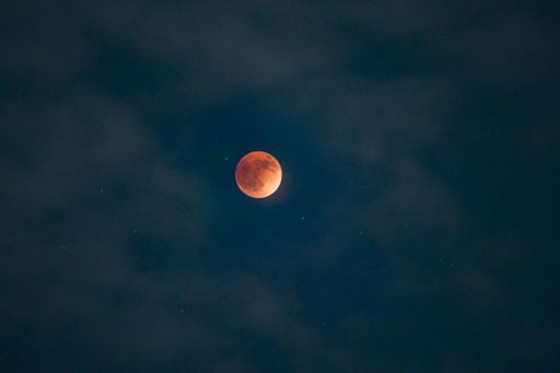A scenic view of the Moon shining vibrantly in the night sky enveloped in clouds