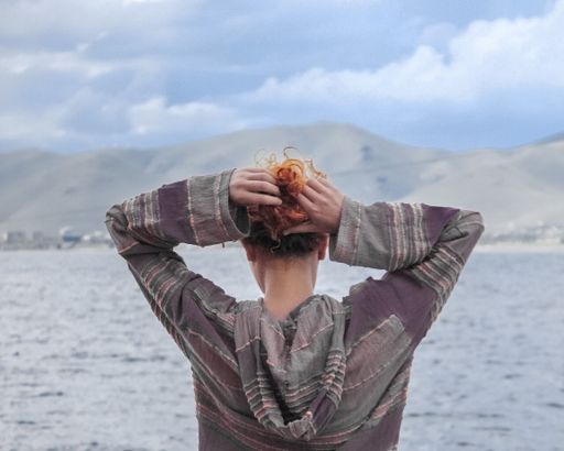 A closeup of a girl from behind with a lake and mountains in the background