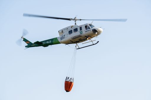 ronda,malaga,spain june 11, 2022 firefighting helicopter in mid-flight dropping water bag on flames