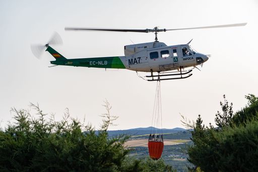 ronda,malaga,spain june 11, 2022 firefighting helicopter in mid-flight dropping water bag on flames