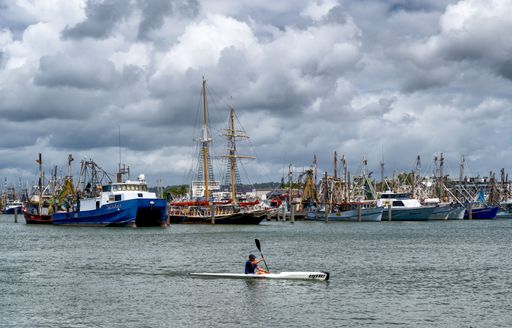 A lonely kayaker paddling in front of fishing trawler in Port Mooloolaba, Australia
