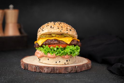 A focus shot of a delicious Angus burger places on a wood placemat in front of a black background.