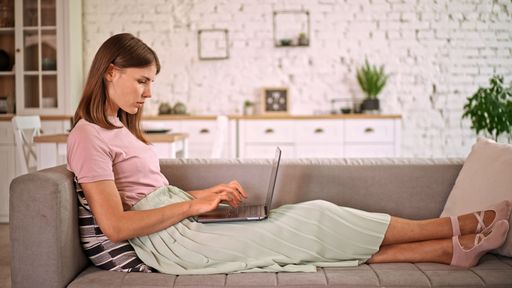 A caucasian business woman lying on a sofa and working on laptop