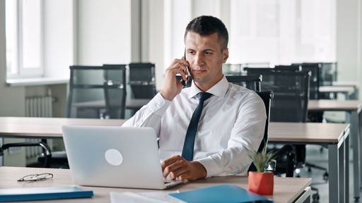 A Caucasian businessman working on laptop and talking on the phone in the office