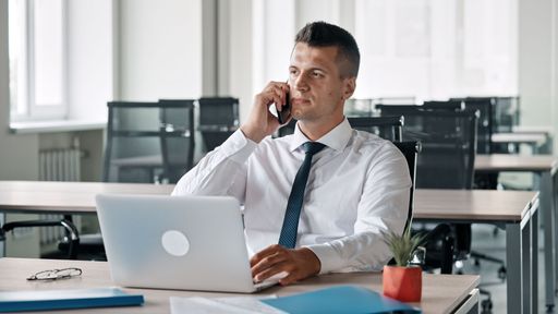 A Caucasian businessman working on laptop and talking on the phone in the office