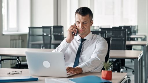 A Caucasian businessman working on laptop and talking on the phone in the office
