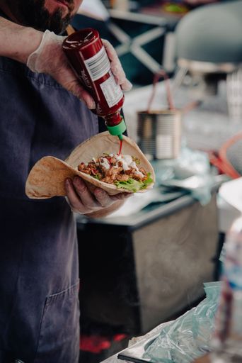 A vertical shot of a chef pouting ketchup on tacos during a food festivel