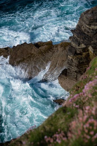 An aerial view of sea waves crashing into the rocky cliff in Cornwall, UK