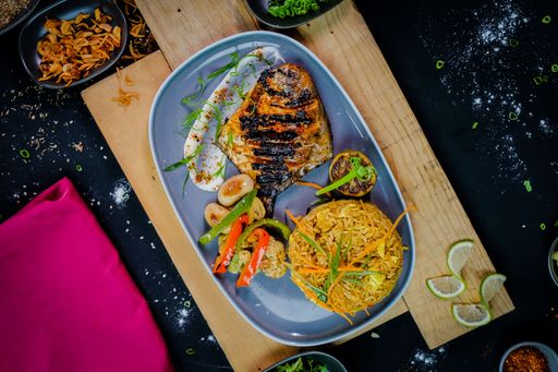 A top view of grilled fish with vegetables and rice served on a blue plate
