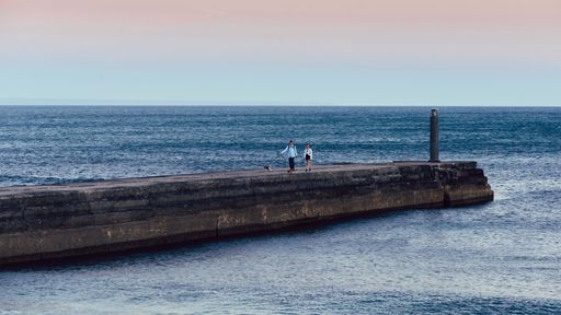 A man and woman walking dogs on a pier at sunset in Cascais, Portugal