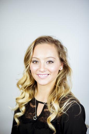 A portrait of a smiling blonde girl under the lights against a white background