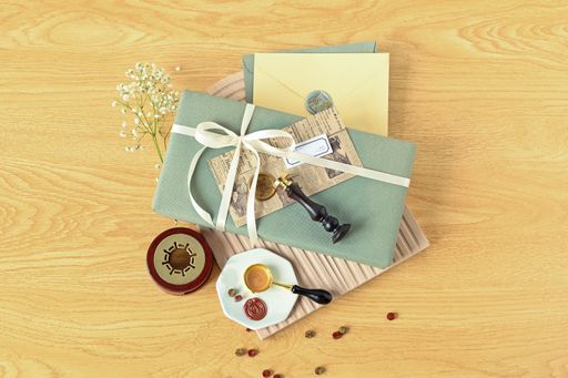 A flat lay of a wrapped gift, envelopes and wax stamp supplies on a wooden table