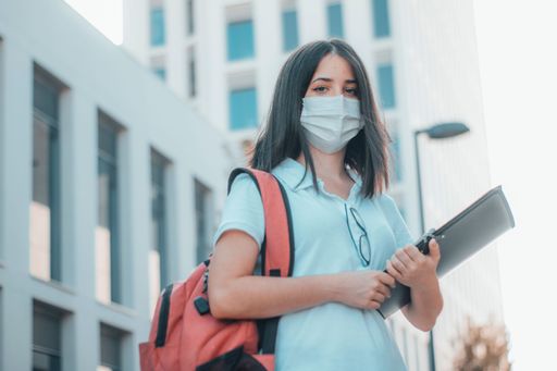 A low angle shot of a white Caucasian woman with a backpack and drawing kit wearing a face mask.