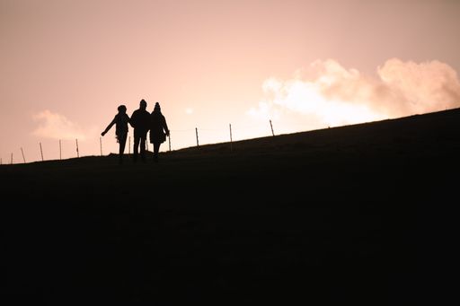 Three people in silhouette walking along the top of the South Downs, East Sussex, UK