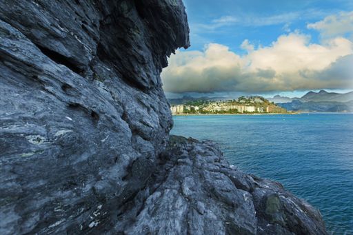 A breathtaking scenery of a seashore with big rocks and a view to the island under the cloudy sky in Spain, Almunecar, cliff San Cristobal
