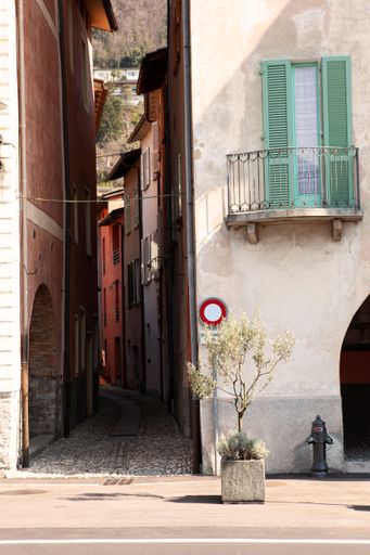 A vertical shot of the building wall with a balcony above the pavement near the narrow footpath.