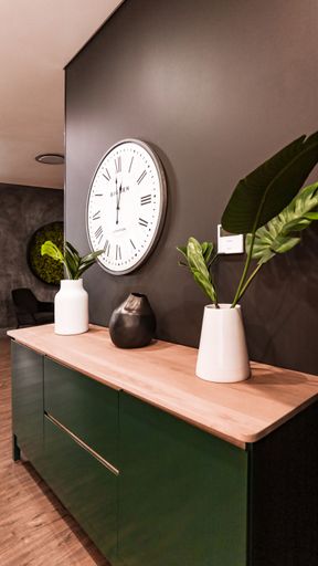 A vertical shot of a green wooden shelf stand with potted plants and a decorative vintage clock