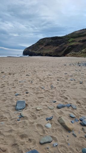 A vertical shot of some of rocks on the beach and a cliff with sea in the background