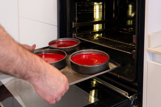 Hands of a man putting the raw red velvet cake in the oven, cooking a red velvet cake in the kitchen at home