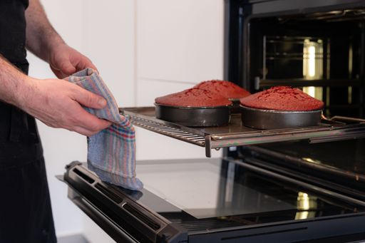 A man baker cooking a red velvet cake in the kitchen at home, taking the baked cake out of the oven pans