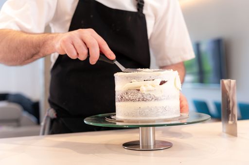 A man cooking a red velvet cake at home, adding the cream with the smoothing spatula leaving the perfect circle