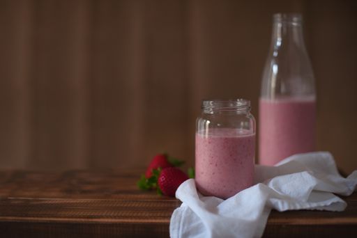 A closeup of a jar of strawberry smoothie on the table with a bottle on the background