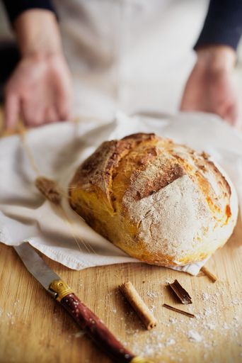 A vertical shot of a loaf of bread on a napkin with a baker on the blurry background