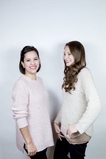 A vertical shot of two female standing near each other and laughing with a white background