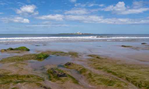 A scenic view of an island in a sea against a rocky beach under a  cloudy blue sky